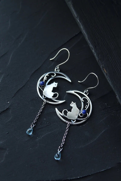 Close-up of alloy crescent moon cat charm dangle earring showing chain and blue bead drop detail