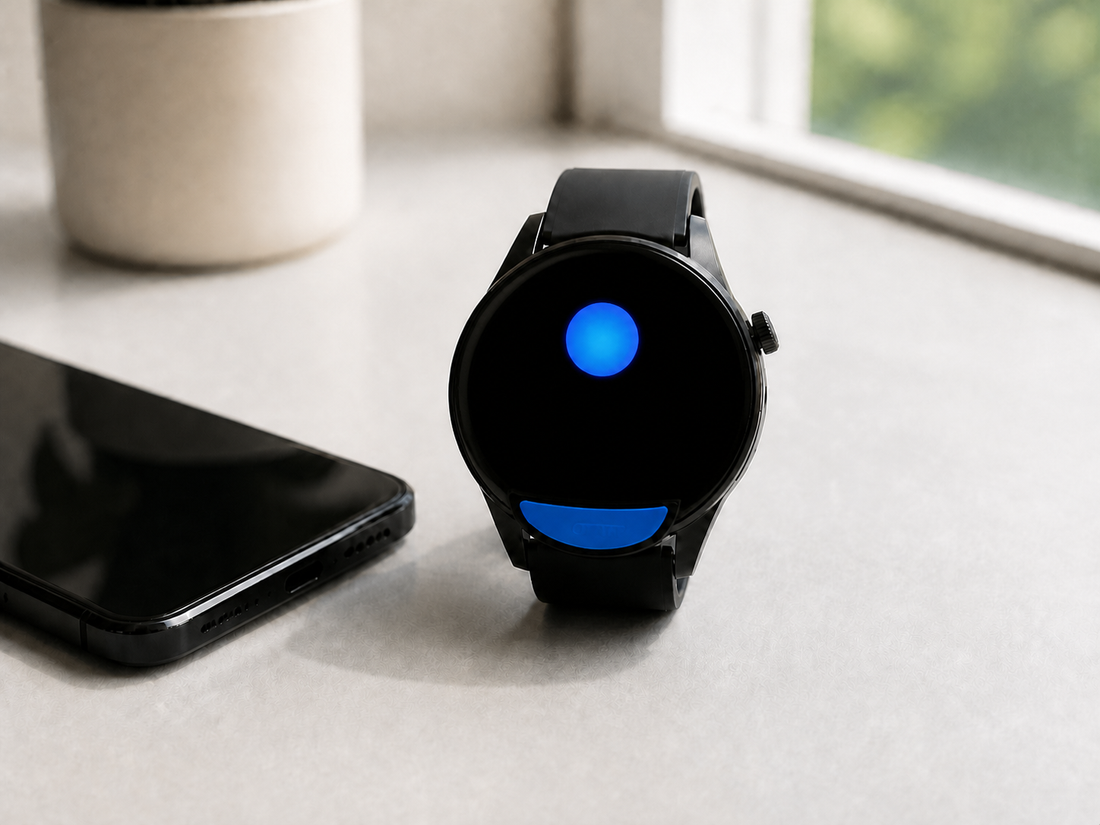 Black round Bluetooth smartwatch beside a phone on a bright desk
