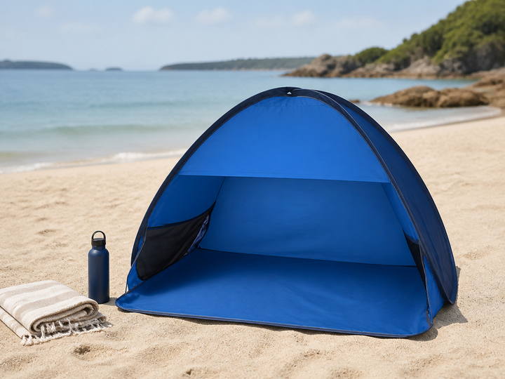 Blue pop-up beach tent set up on sand beside calm water