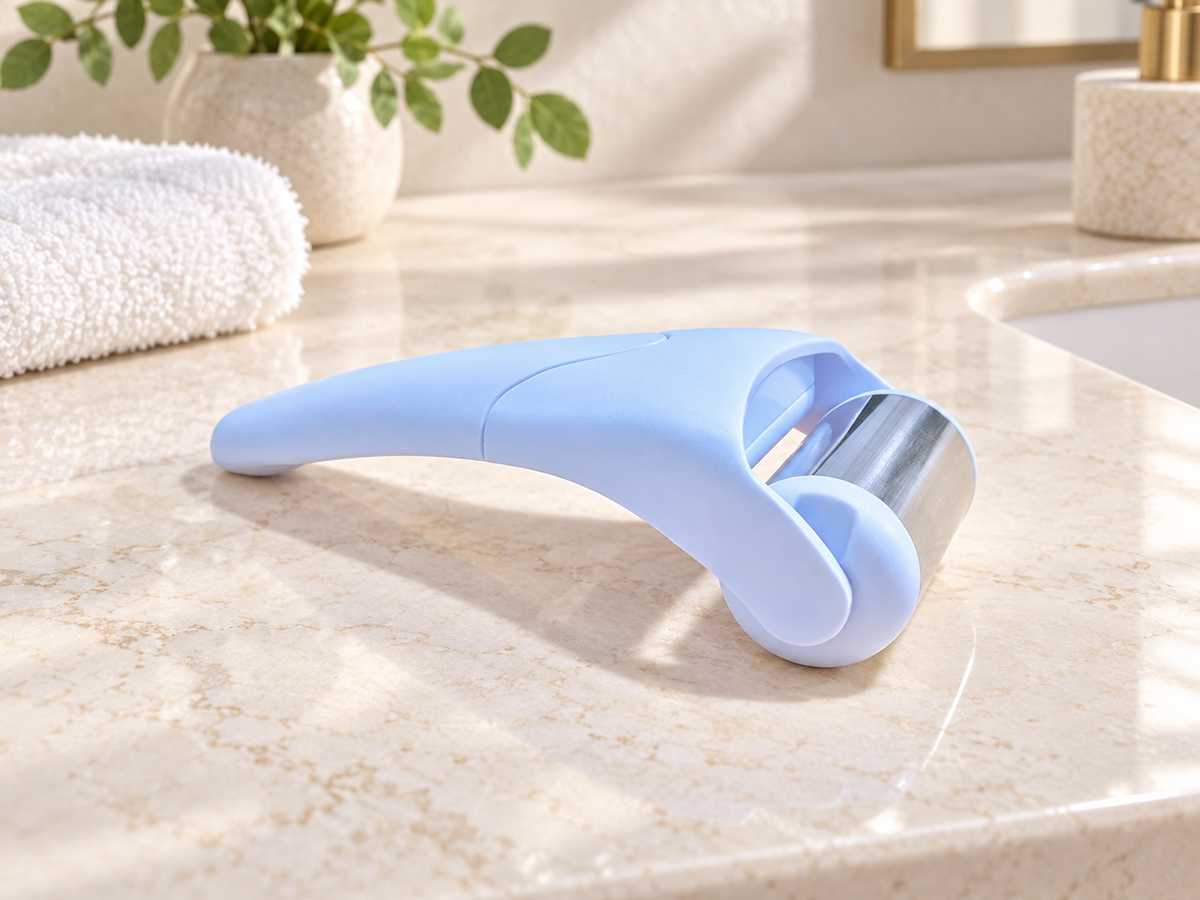 Light blue stainless steel facial ice roller on a sunlit bathroom vanity
