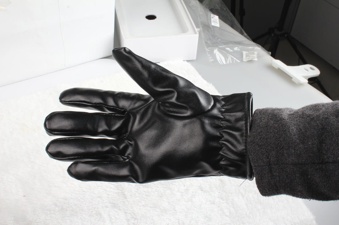 Hand wearing a black faux leather glove next to a laptop