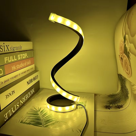 Black spiral lamp glowing warm yellow next to a stack of books