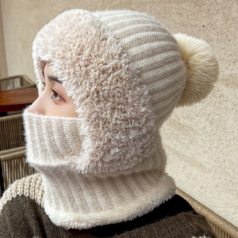 Woman wearing a beige knit hat-scarf hood with pom pom pulled up over her nose