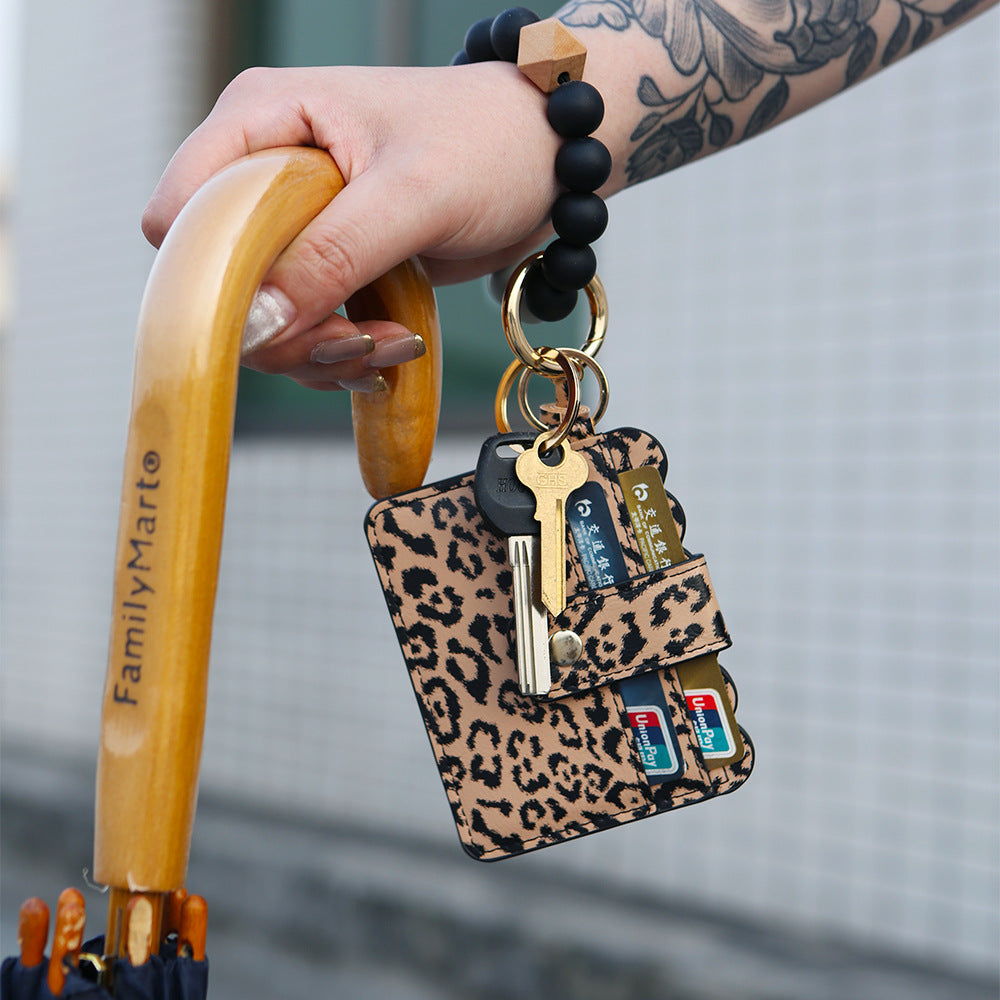 Hand holding a leopard print wristlet keychain with keys and card pouch