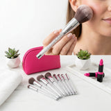 Woman applying powder with a large makeup brush with a clear crystal handle next to a pink zippered brush case