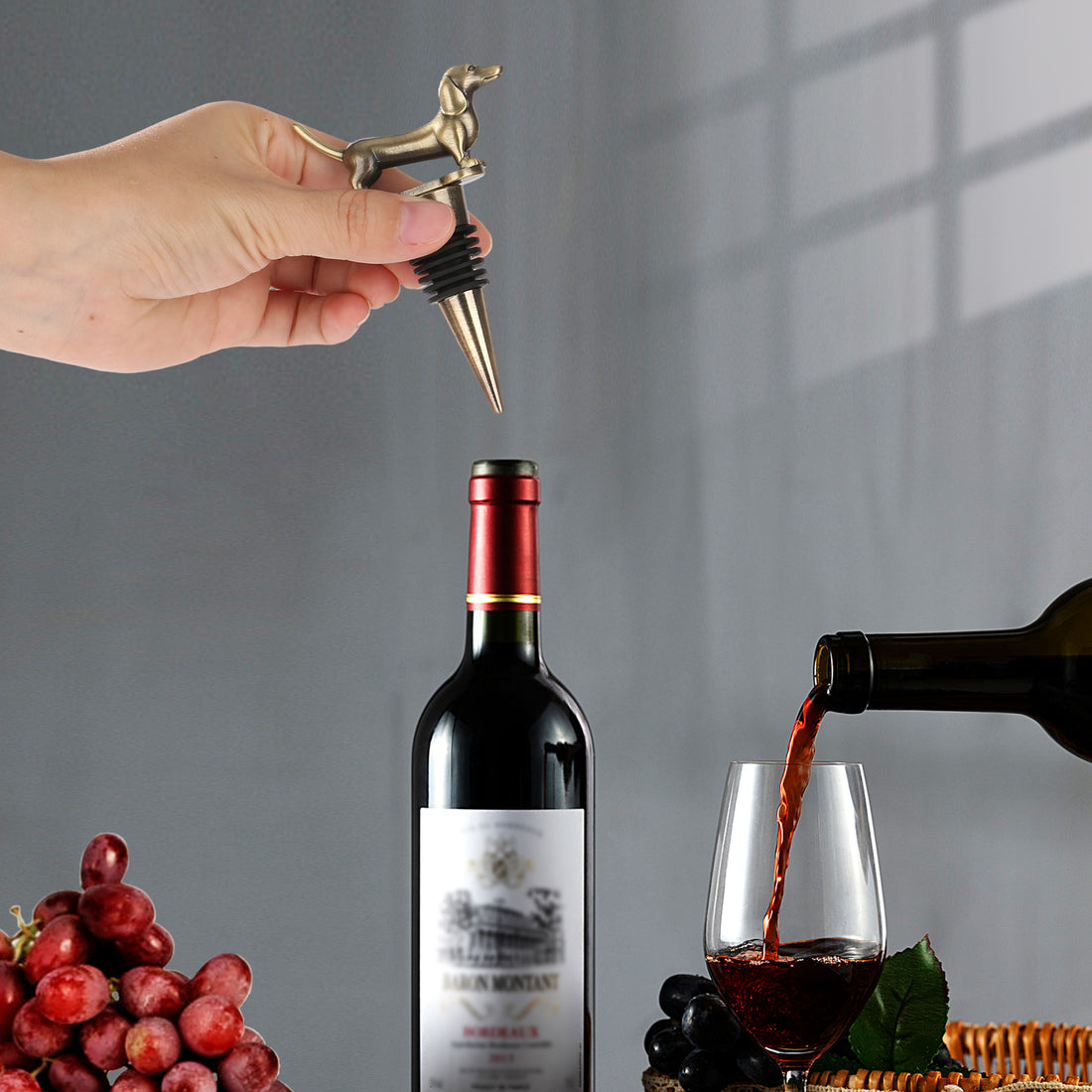 Hand holding a gold dachshund stopper over a red wine bottle