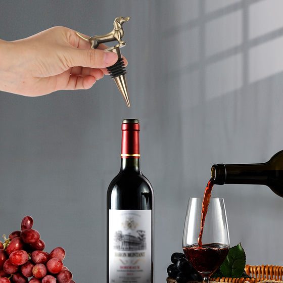 Hand holding a gold dachshund stopper over a red wine bottle