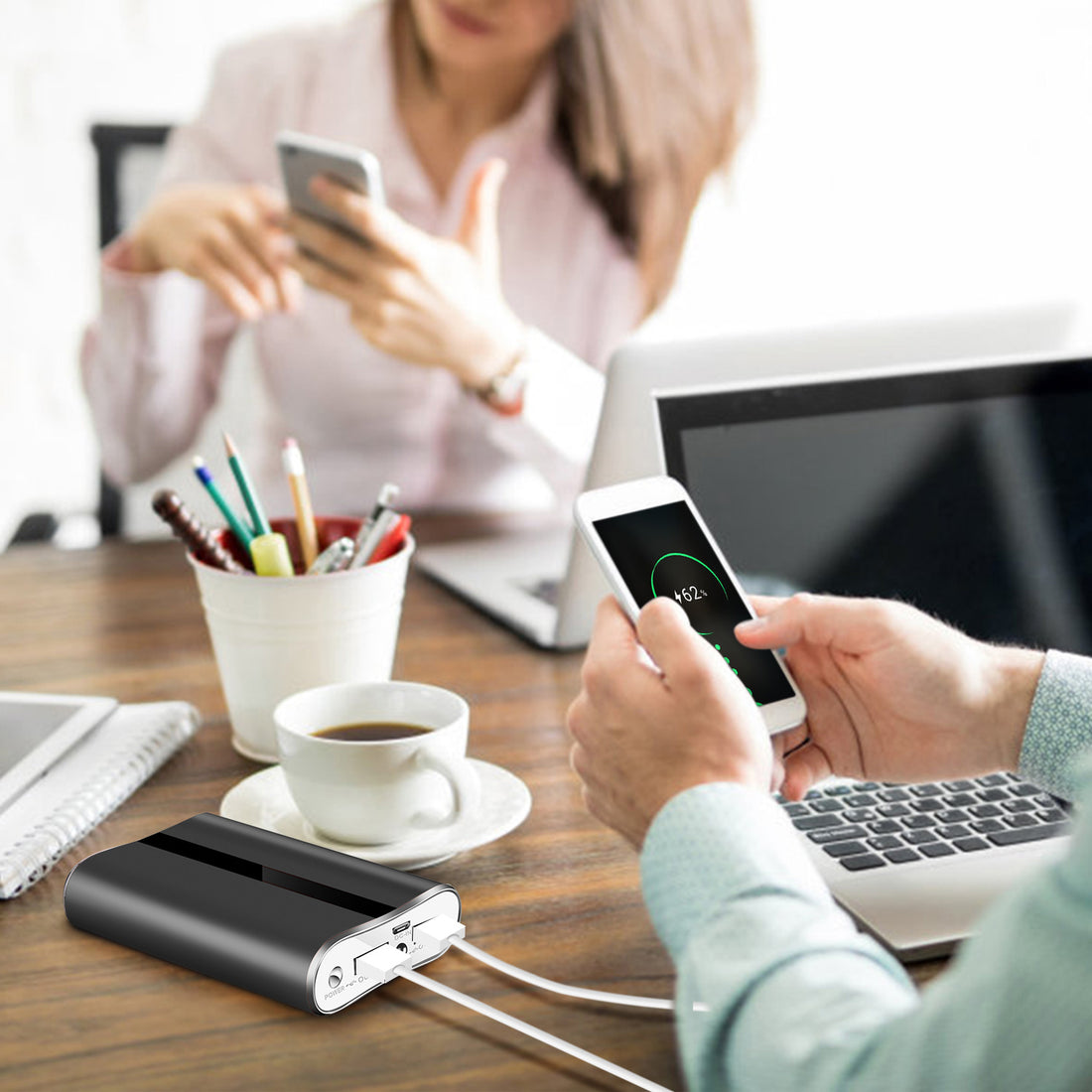 Power bank charging a phone on a desk next to a coffee cup