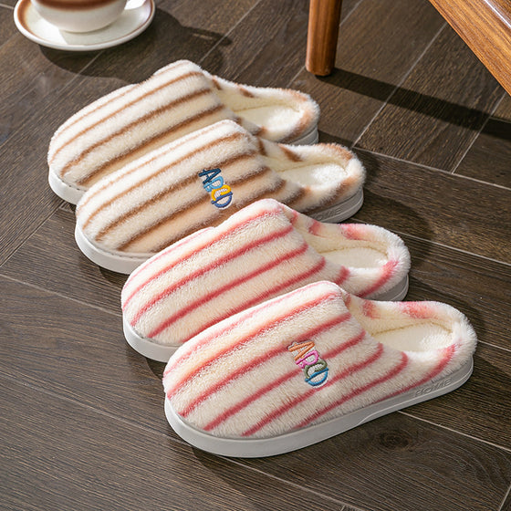 Striped plush slippers in coffee, pink and other colors on a wooden floor