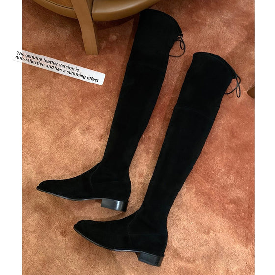 Black over-the-knee suede boots with a lace-up back on a rug