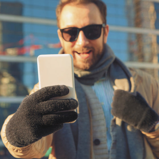 Man in sunglasses taking a selfie while wearing black knit gloves