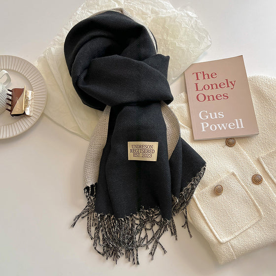 Black and gray double-sided scarf with tassels next to a book