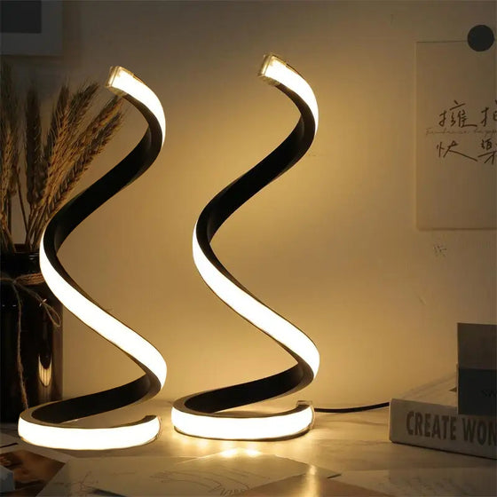 Two black spiral LED lamps glowing warm white on a desk