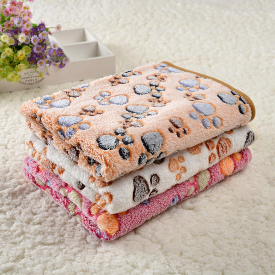 Three folded paw print pet blankets in tan, cream and pink