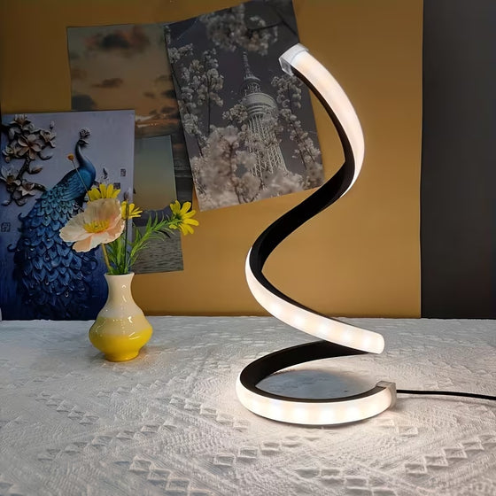 Black spiral LED lamp glowing white next to a vase of flowers