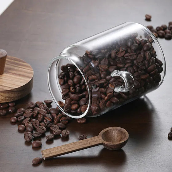 Tipped glass coffee jar spilling beans beside a wooden spoon