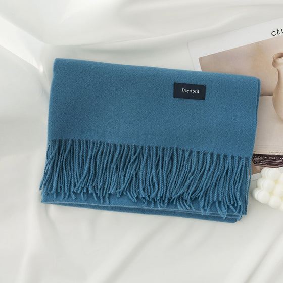 Blue faux cashmere scarf with tassels folded on white bedding
