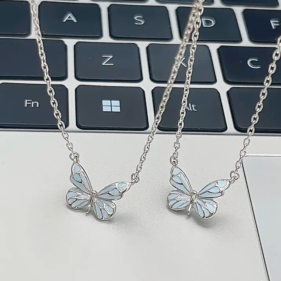 Two butterfly pendant necklaces on a laptop keyboard, not included