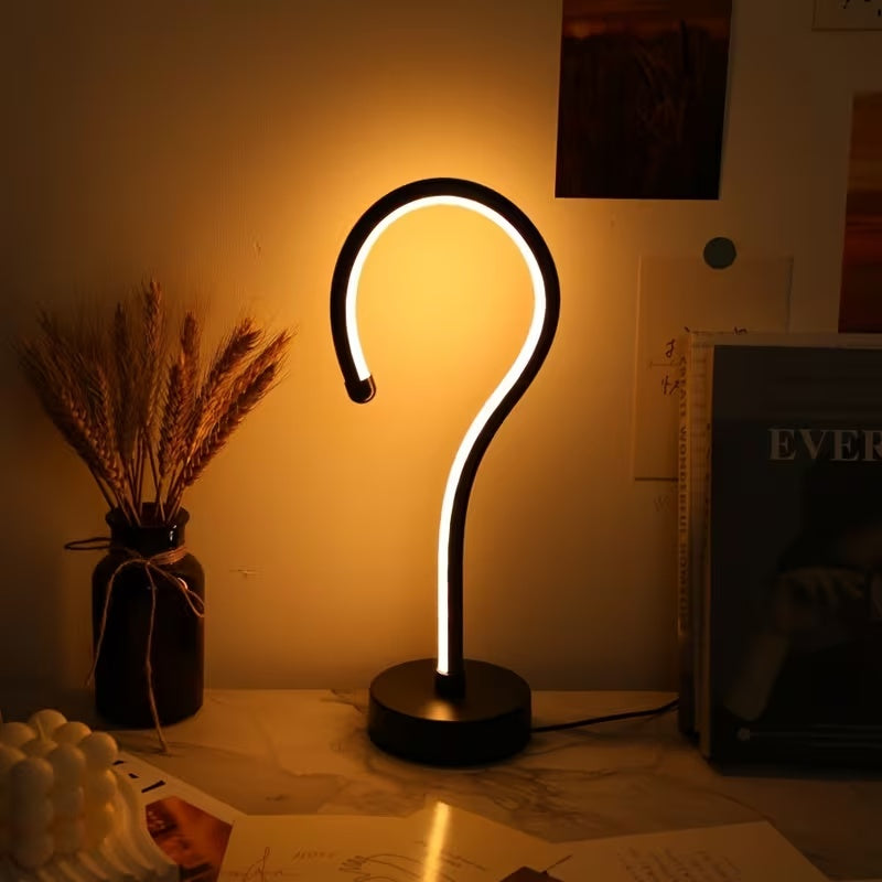 Question mark lamp glowing warm white on a desk with dried flowers