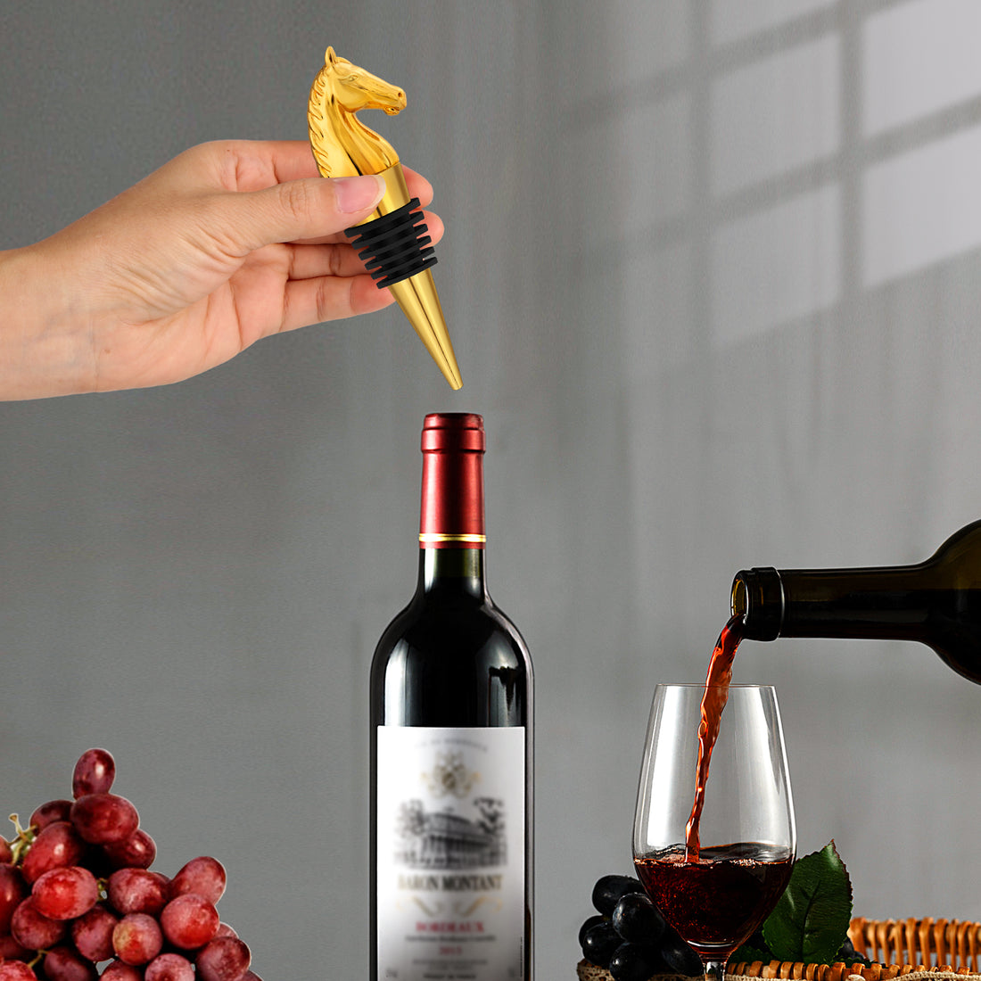 Hand holding a gold horse head stopper over a red wine bottle