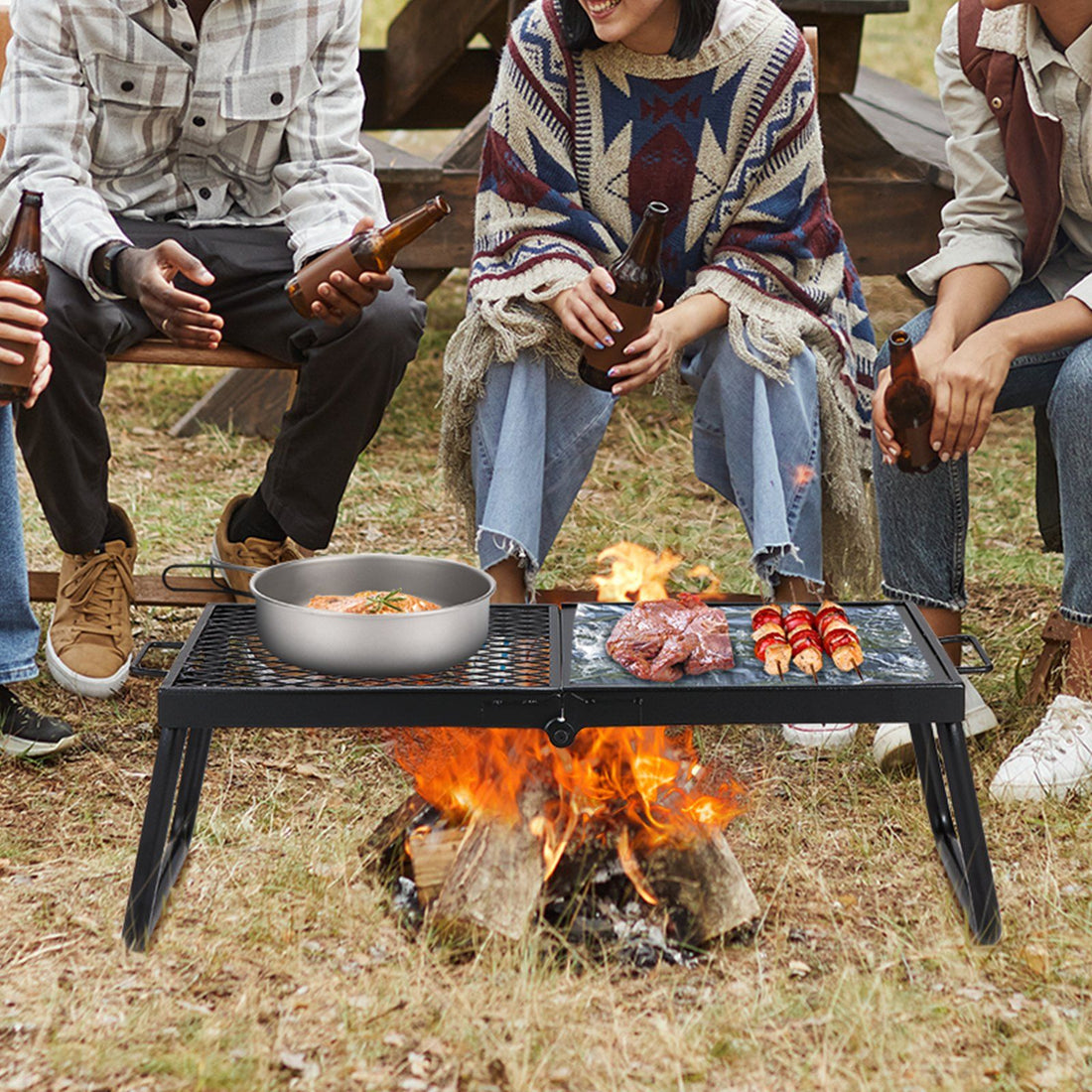 Black folding campfire grill with a flat griddle section and a wire grate section over an open flame