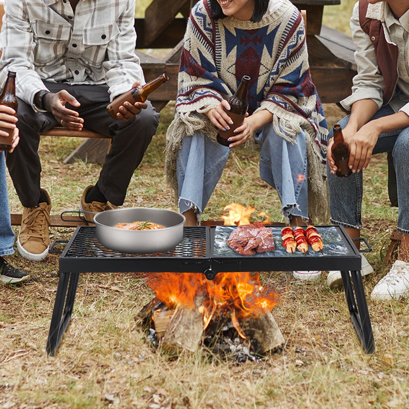 Black folding campfire grill with a flat griddle section and a wire grate section over an open flame