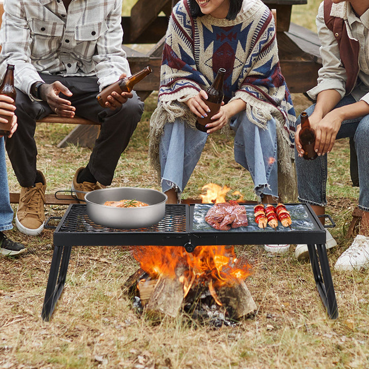 Black folding campfire grill with a flat griddle section and a wire grate section over an open flame