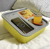 Yellow snack tray with wireless phone charger, USB ports, snack bowl, and cup holder on a bed