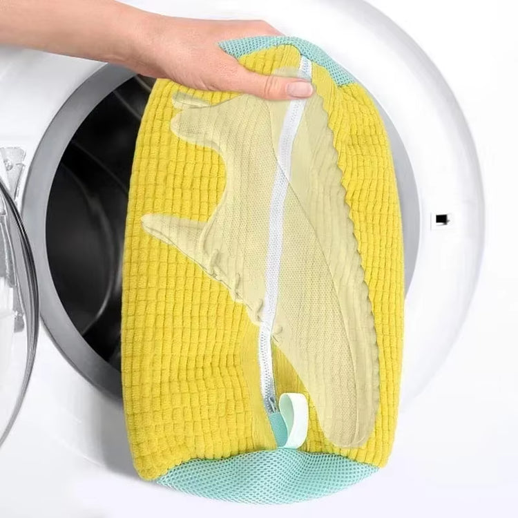 Yellow zippered mesh laundry bag holding a sneaker, held open at a front-load washing machine door