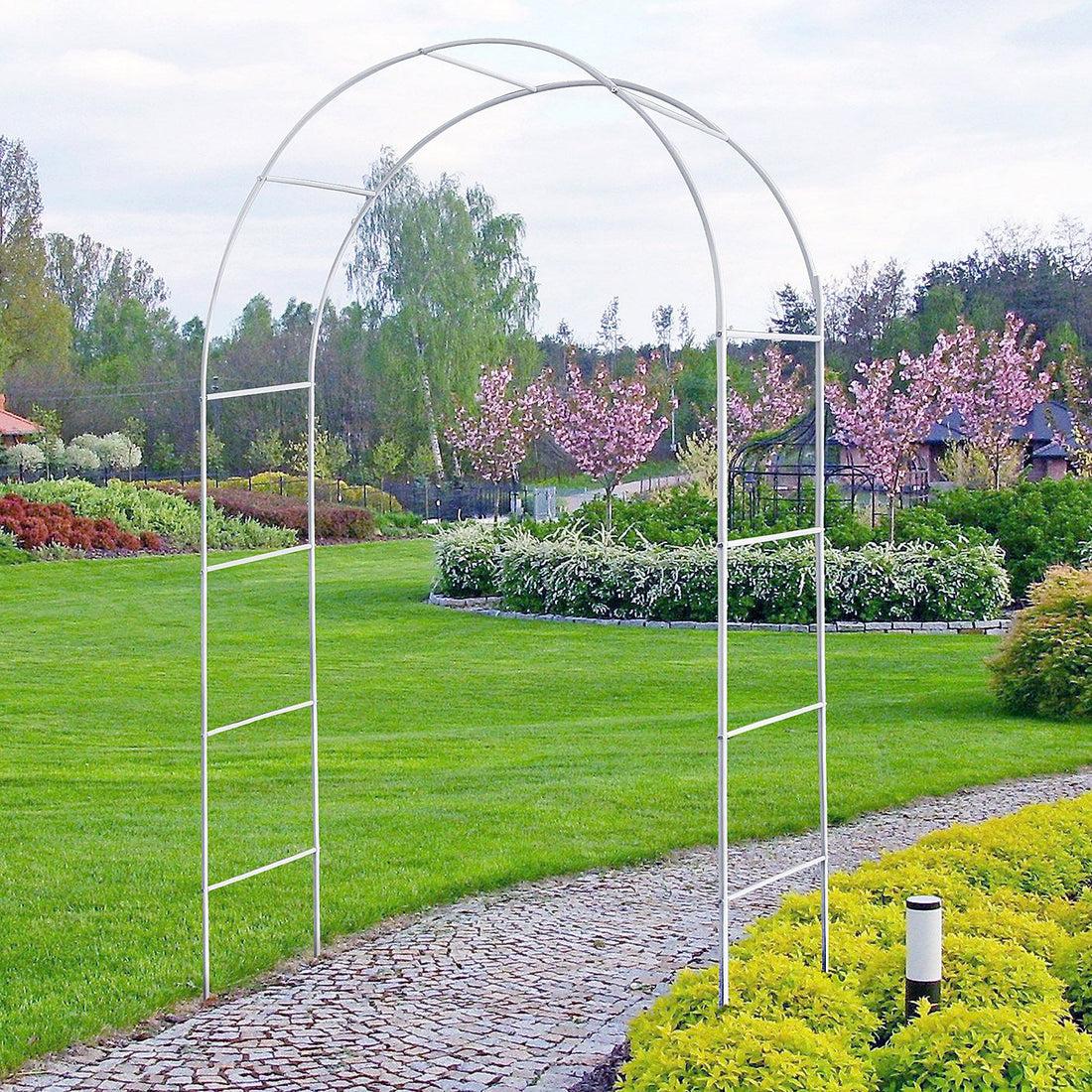 White metal garden arch trellis arbor with climbing plants over walkway