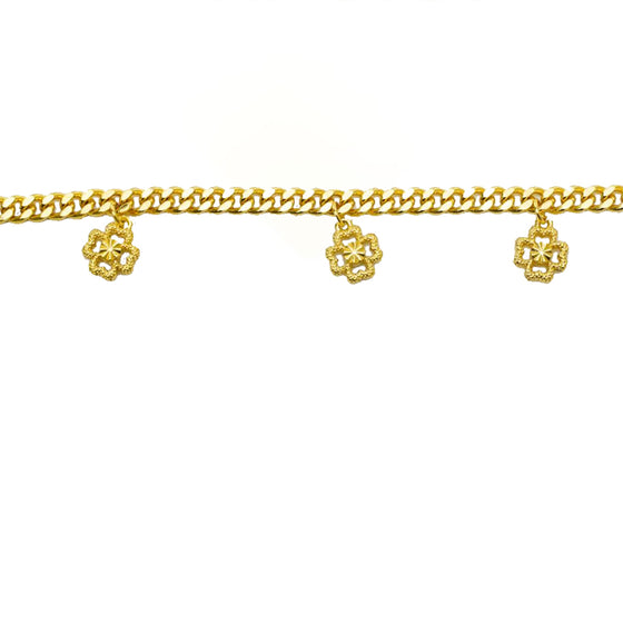 Gold curb chain bracelet with clover charms laid straight, close-up