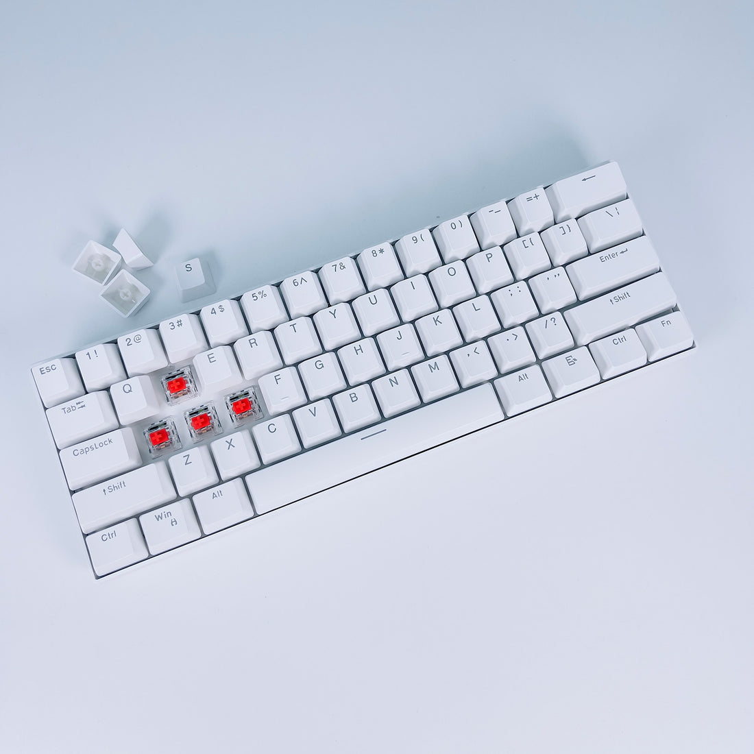 White 60% mechanical keyboard with keycaps removed showing red switches