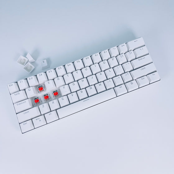 White 60% mechanical keyboard with keycaps removed showing red switches