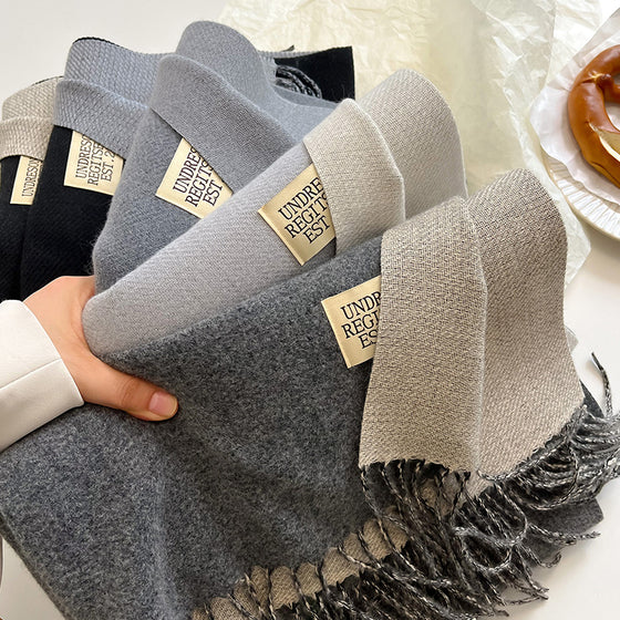 Hand holding several gray two-tone faux cashmere scarves