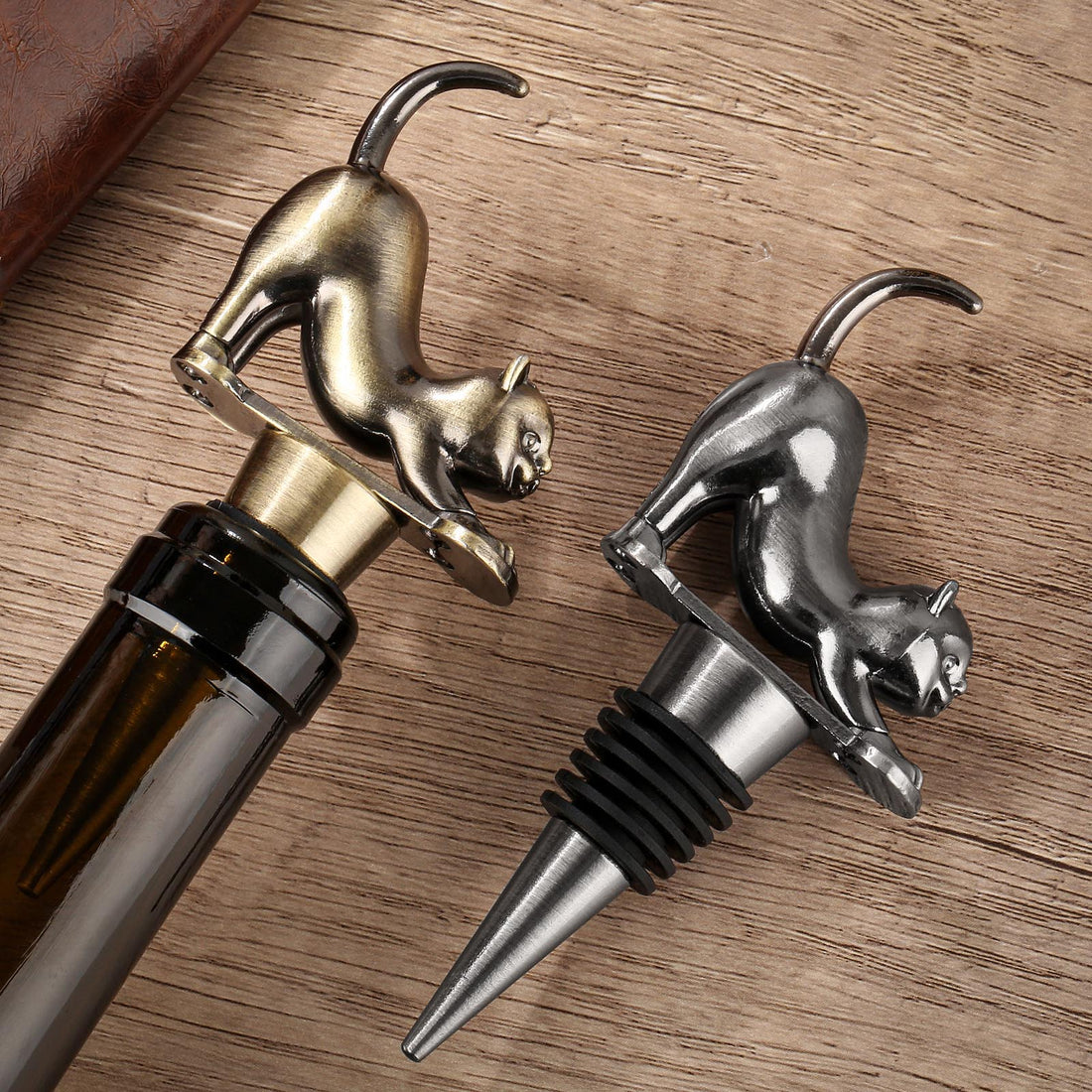 Bronze and dark silver cat wine stoppers in wine bottles on a wooden table