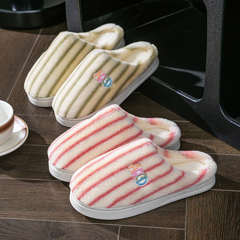 Green and pink striped plush slippers on a wooden floor