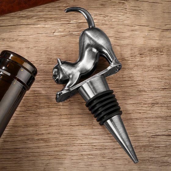 Dark silver cat-shaped wine stopper resting on a wine bottle neck, wood table