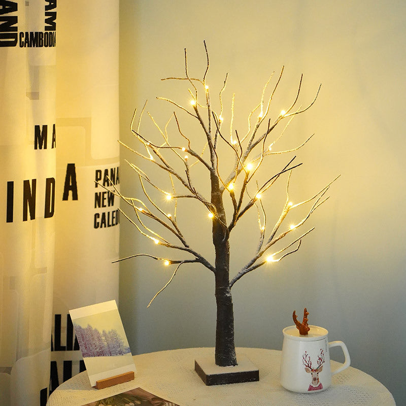 Snow-dusted LED birch tree light glowing on a shelf beside a sign