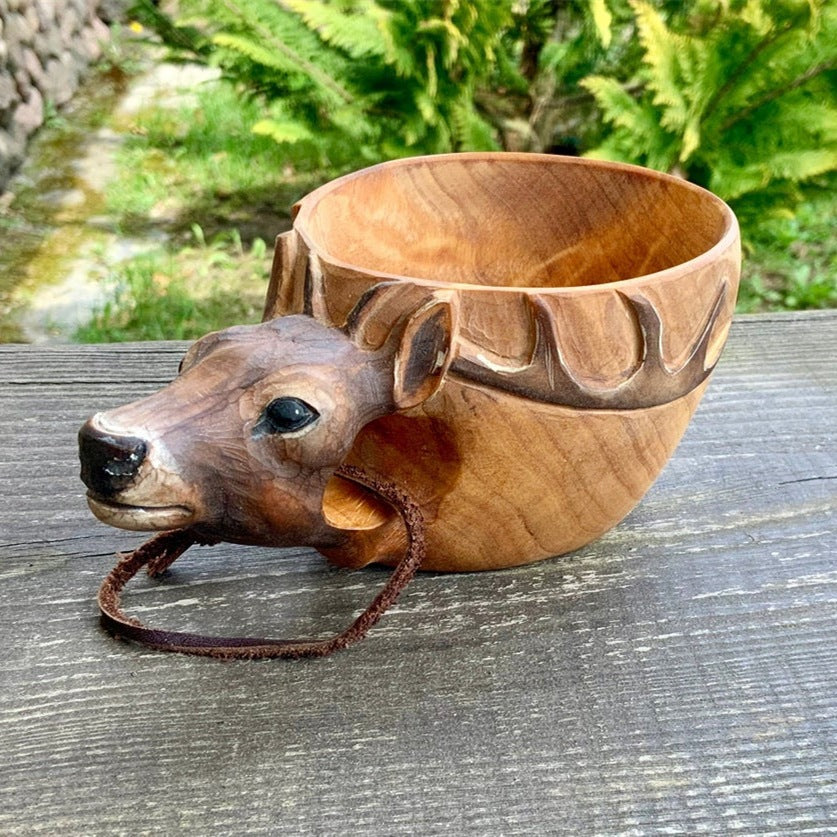 Kuksa wooden mug with carved elk head and antler handle on a picnic table