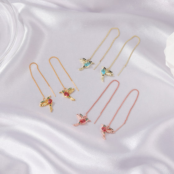 Three pairs of hummingbird earrings on white satin