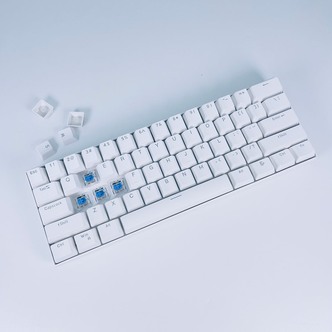 White 60% mechanical keyboard with keycaps removed showing blue switches