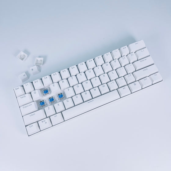 White 60% mechanical keyboard with keycaps removed showing blue switches