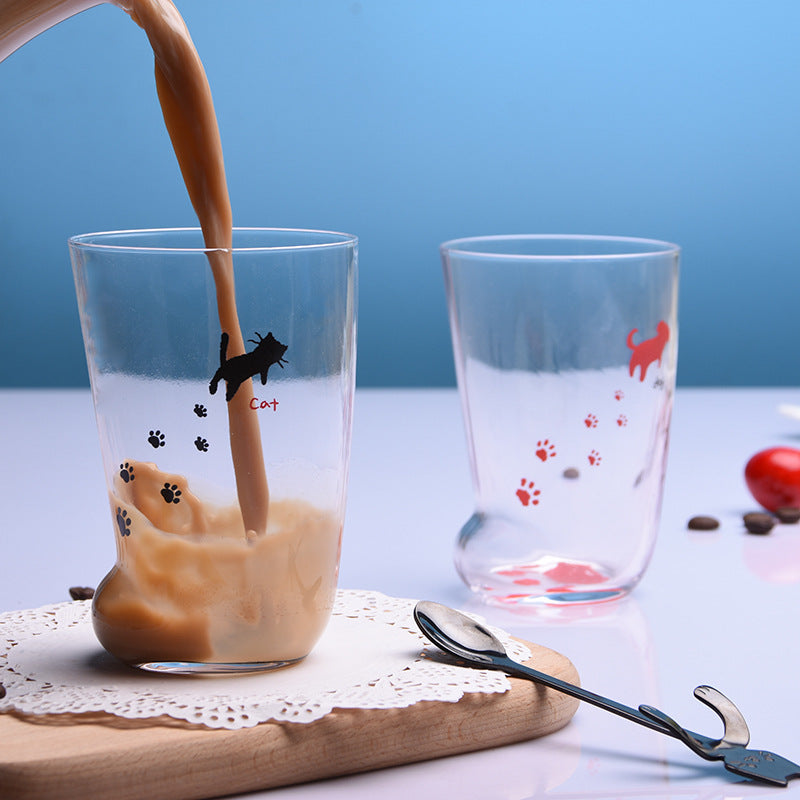Coffee being poured into a cat paw glass mug beside a paw print cup