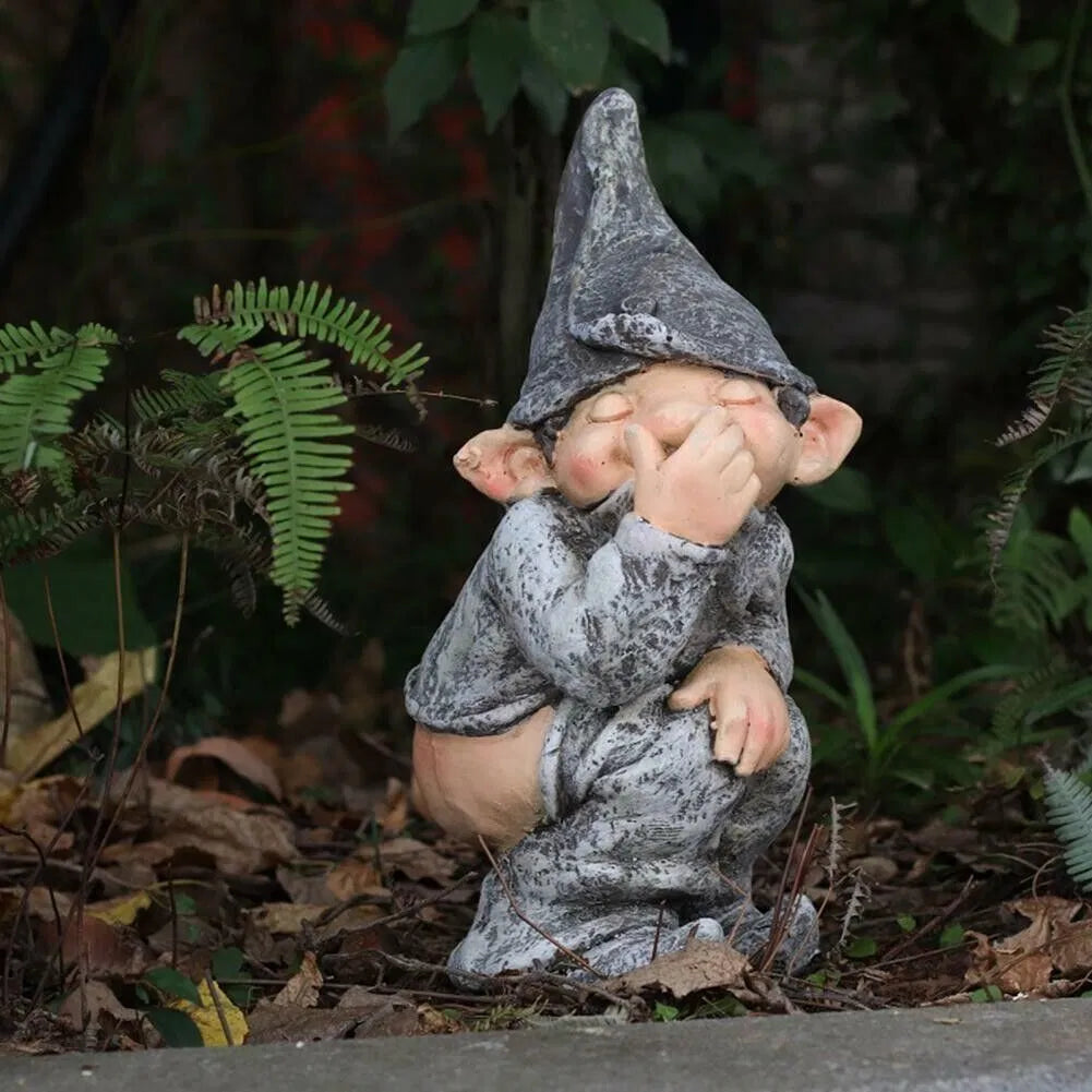 Pooping garden gnome statue among ferns in a garden bed