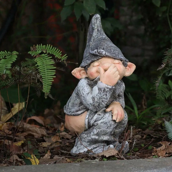 Pooping garden gnome statue among ferns in a garden bed