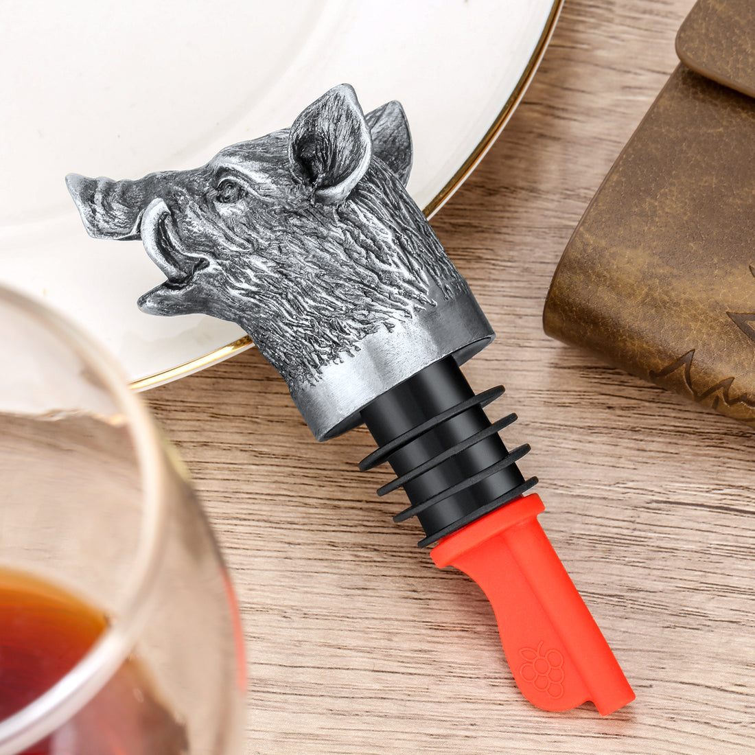 Dark silver wild boar head pourer with red spout lying on a wooden table