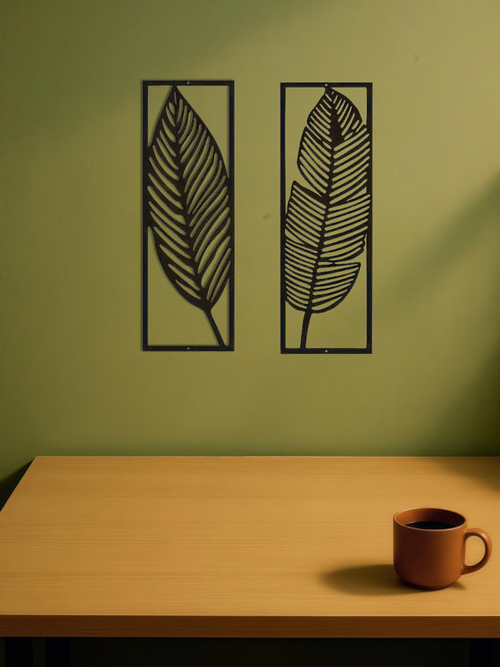 Two black metal leaf panels on a green wall above a table