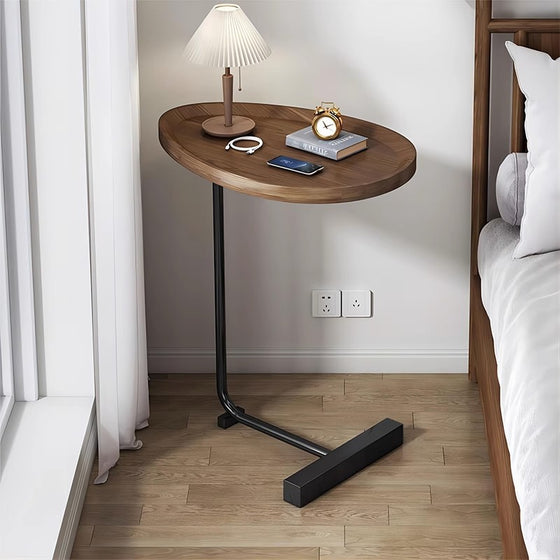 Oval walnut table with a black C-shaped frame beside a bed