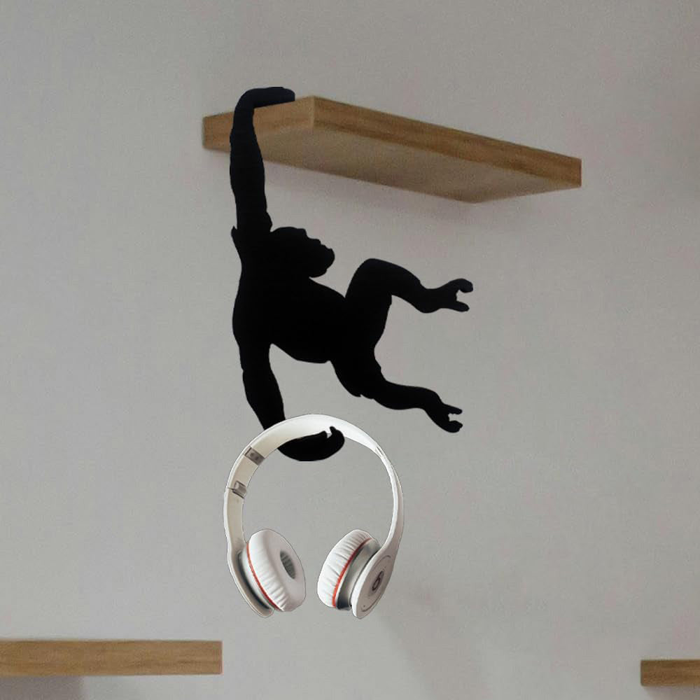 Monkey wall hook holding white headphones under a floating shelf