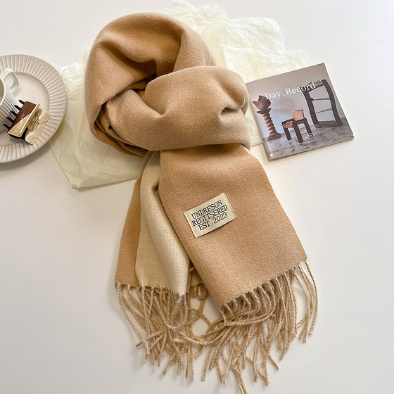 Camel and cream two-tone faux cashmere scarf with tassels on a table